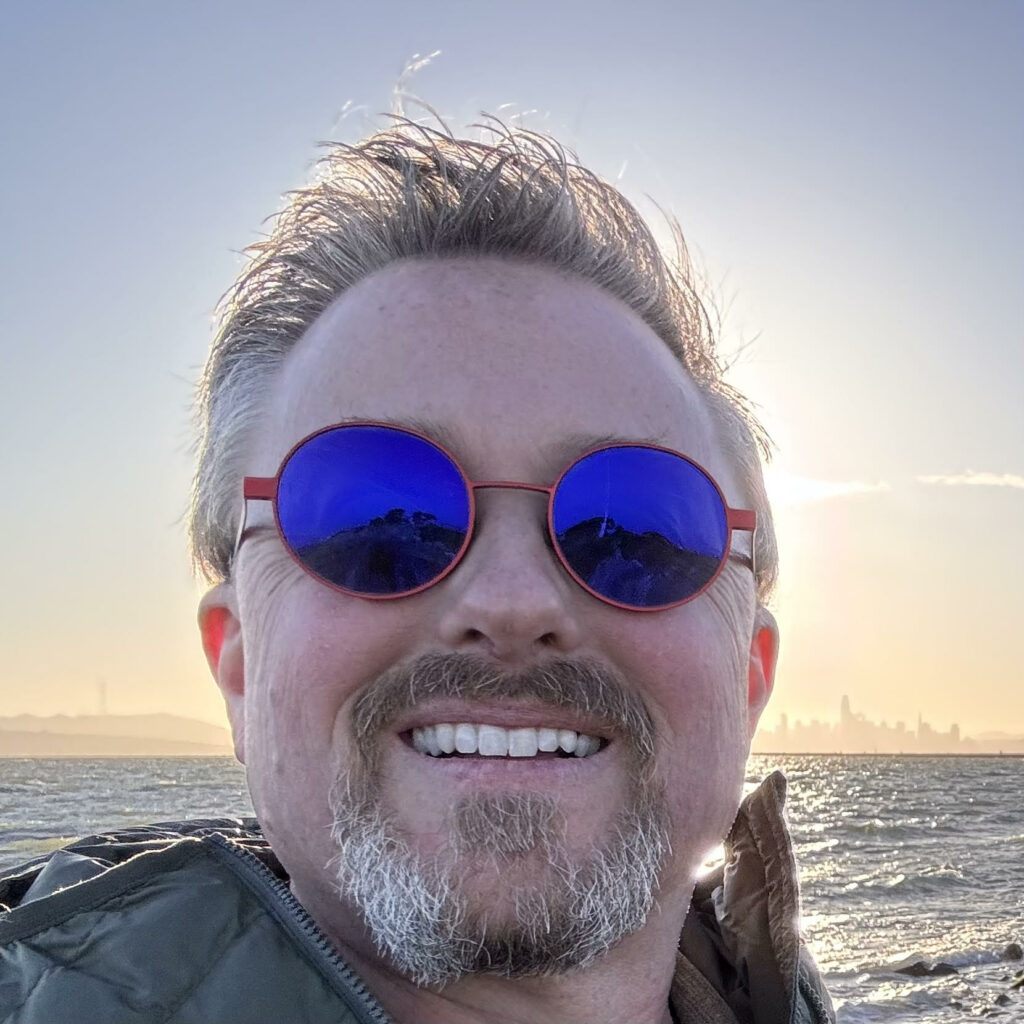 Greg in Alameda, California with the San Francisco cityscape behind him at sunset.